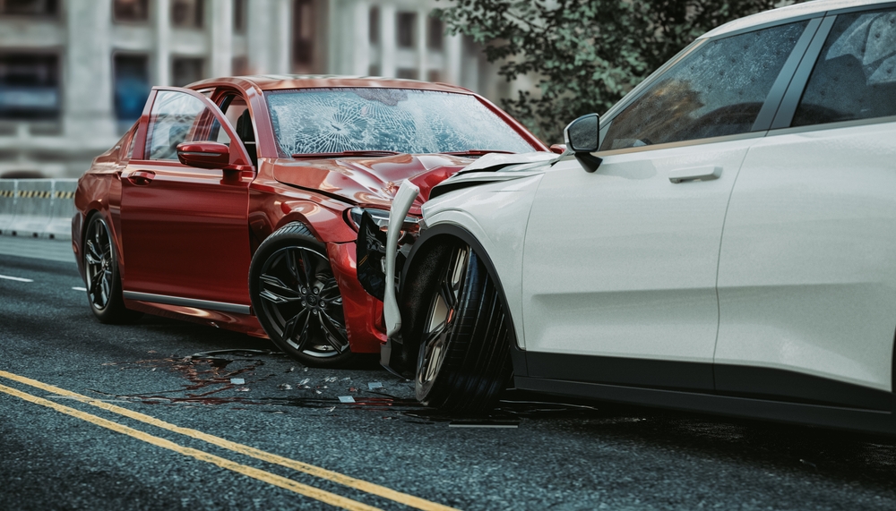 Two severely damaged cars involved in a head-on collision on a city street, showing crumpled front ends and broken glass.