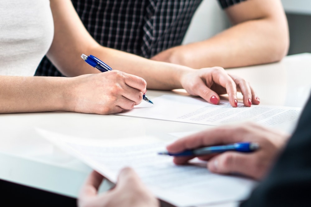 Close-up of people sitting at a table reviewing and signing documents, representing how insurance companies calculate injury settlements.