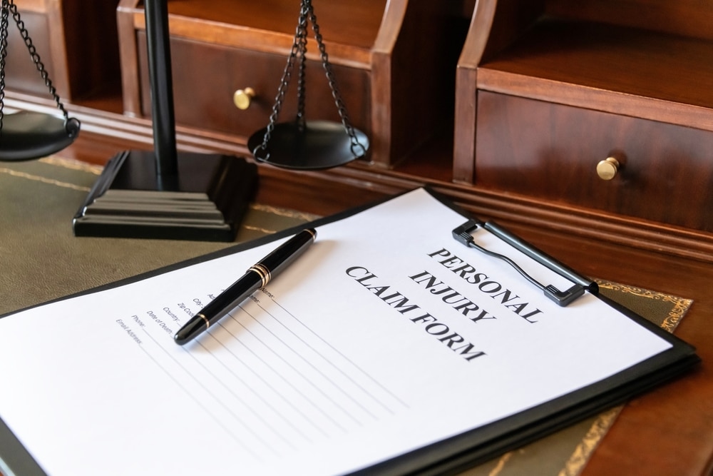 Personal injury claim form and pen on a lawyer’s desk beside scales of justice.